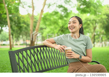 Happy female enjoying leisure time outdoors with a hot drink in hand 130599905