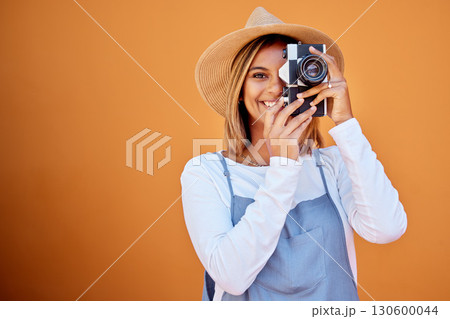 Photographer, portrait and woman shooting a picture or photo with a retro camera isolated in an orange background. Happy, studio and female taking creative shots or fashion photographs as photography 130600044