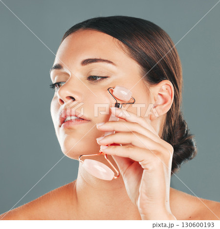 Face massage closeup with roller, woman and skincare, beauty and healthy skin isolated on studio background. Natural cosmetics, glow and rose quartz makeup tools in hand, manicure and cosmetic care 130600193