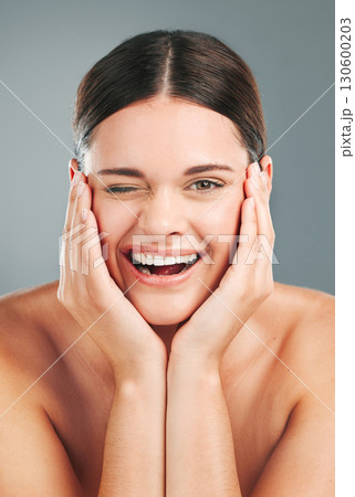 Beauty, wellness and portrait of woman wink on gray background for cosmetics, facial treatment and spa. Dermatology, skincare and face of happy girl for glow, healthy skin and natural smile in studio 130600203