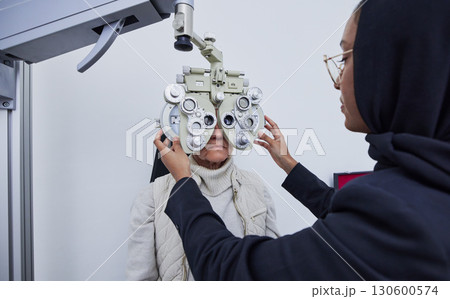 Eye exam, optometry consultation and woman test for medical, healthcare and vision with muslim expert. Eyes check or consulting of senior person and professional optometrist with phoropter machine 130600574