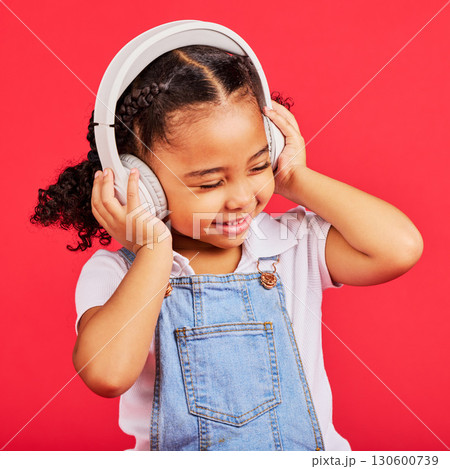 Happy, child and headphones for music, radio and fun podcast on isolated red background and dancing studio. Smile, little girl and kid listening to dance audio, song and streaming media on backdrop 130600739