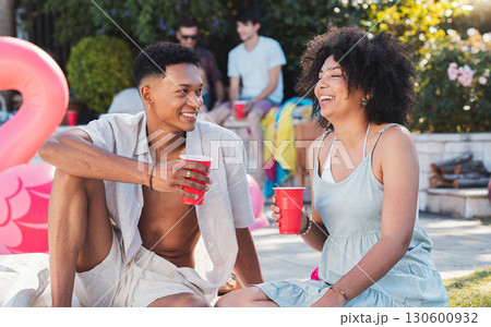 Summer, pool party and couple of friends with drinks outdoor with social celebration and happiness. Event, alcohol and young people relax on the floor talking with friend communication laughing Summer, pool party and couple of friends with drinks outdoor with social celebration and happiness. Event, alcohol and young people relax on the floor talking with friend communication laughing 130600932