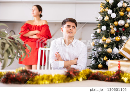 Upset young couple arguing among themselves before X-mas Eve near Christmas tree in kitchen at home Upset young couple arguing among themselves before X-mas Eve near Christmas tree in kitchen at home 130601193