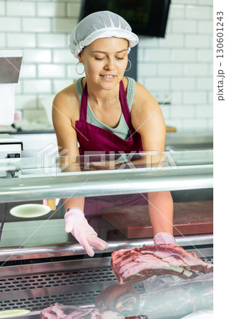 Positive young saleswoman demonstrating piece of meat in butcher shop 130601243