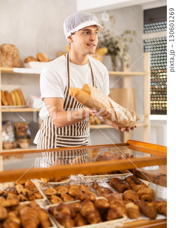 Friendly guy offers to buy hot baguettes to customer in bakery interior 130601269