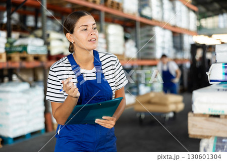 In warehouse of store, girl checks quantity of goods and receipt documents for products In warehouse of store, girl checks quantity of goods and receipt documents for products 130601304