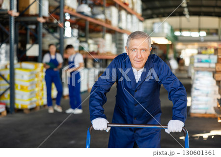 Elderly loader man pushing cart in warehouse Elderly loader man pushing cart in warehouse 130601361