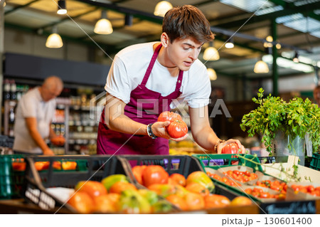 European male seller in apron takes tomatoes from window 130601400