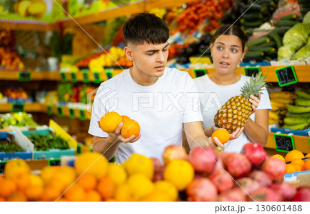 Male and female customers in casual clothes buying pineapples and oranges in grocery store 130601488