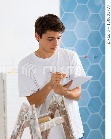 Young designer taking notes on papers while planning interior decoration 130601777