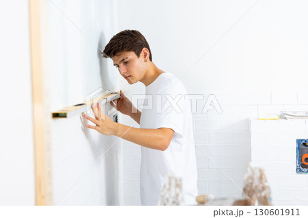 Guy inspecting quality of tiles laid on walls with level meter Guy inspecting quality of tiles laid on walls with level meter 130601911