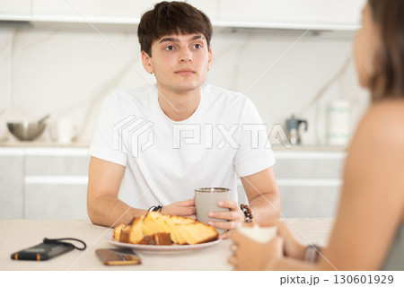 Happy young couple sitting at the kitchen-table and having conversation while drinking tea Happy young couple sitting at the kitchen-table and having conversation while drinking tea 130601929