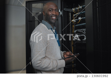 Portrait, server room and IT black man on tablet for database connection cable, maintenance or software update. Cybersecurity, face and male coder with technology for networking in data center. Portrait, server room and IT black man on tablet for database connection cable, maintenance or software update. Cybersecurity, face and male coder with technology for networking in data center. 130601992