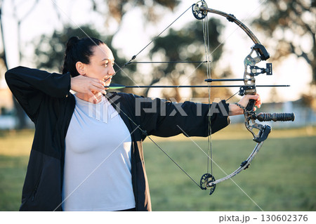 Hobby, learning and woman playing archery as a sport, outdoor activity and game in nature of France. Training, practice and girl with a bow and arrow for sports, competition and shooting at a park 130602376