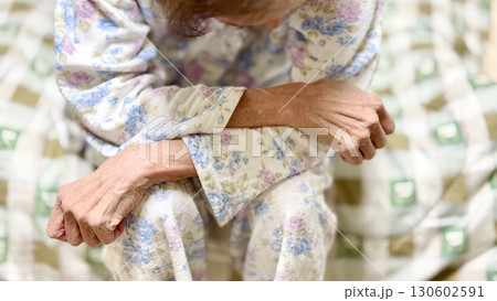 寝巻を着てベッドに座って下向き腕を組む高齢女性 寝巻を着てベッドに座って下向き腕を組む高齢女性 130602591