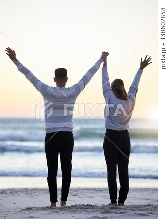 Couple, beach and hands up outdoor while happy at sunset for love, freedom and peace with calm ocean. Young man and woman together on vacation holiday at sea to relax, travel and connect in nature Couple, beach and hands up outdoor while happy at sunset for love, freedom and peace with calm ocean. Young man and woman together on vacation holiday at sea to relax, travel and connect in nature 130602858