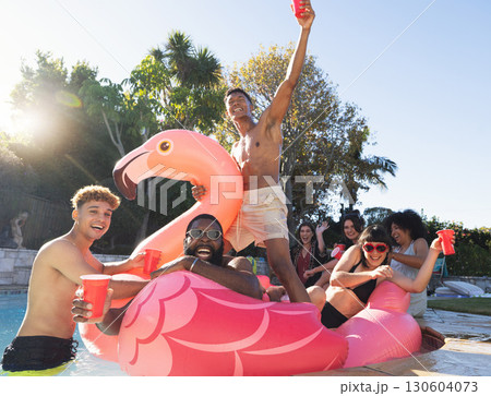 Pool party, beer and friends on flamingo, having fun and partying. Summer celebration, water event and group portrait of drunk funny people laughing with alcohol, swimming and floating on bird float. 130604073