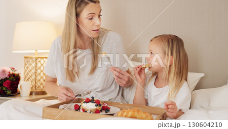 Mother, child and breakfast in the bed together on mothers day, morning and talking in home and eating food or pancakes. Girl, mom and bite of healthy strawberry, croissant or bonding in bedroom 130604210