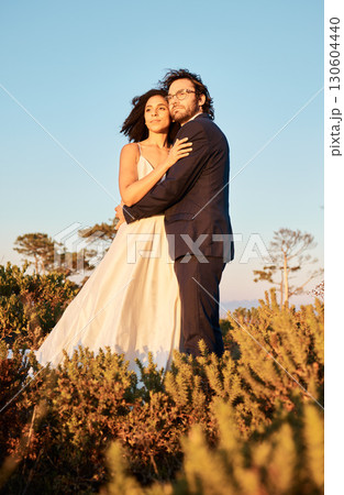 Interracial couple, love and wedding at sunset, hug and happy for romance and relationship in nature. Marriage, bride and groom hug at outdoor ceremony and sweet on blue sky background space Interracial couple, love and wedding at sunset, hug and happy for romance and relationship in nature. Marriage, bride and groom hug at outdoor ceremony and sweet on blue sky background space 130604440