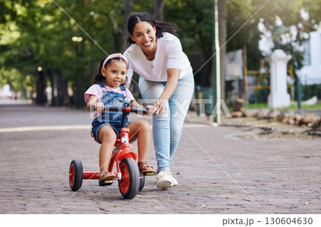 Mother, kid and bicycle teaching with training wheels for learning, practice or safety at the park. Happy mom helping little girl to ride a bike with smile for proud playful moments in the outdoors 130604630