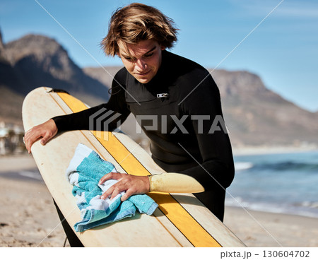 Surfing, man with surfboard on beach with fitness and travel, cleaning board and surf maintenance with extreme sport outdoor. Ocean. nature and workout, young surfer lifestyle and sports motivation 130604702