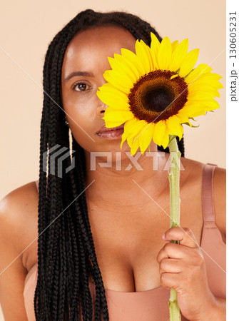 Portrait, beauty and sunflower with a black woman in studio on a beige background for natural treatment or body positivity. Spring, flower and skincare with a young female posing for wellness 130605231