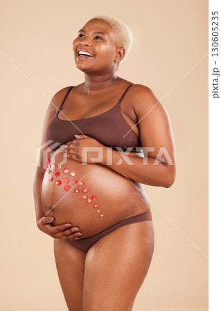 Pregnant, black woman and smile with flowers on belly in studio for body, baby wellness and ivf healthcare. Mother, pregnancy and floral plants on stomach with happiness, beauty or natural childbirth 130605235