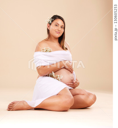 Pregnancy, beauty and portrait of a woman in studio with chiffon material and flowers holding her stomach. Maternity, prenatal health and pregnant female model with floral posing by beige background. 130605253