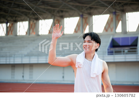 An asian man in white tank top is smiling and waving a hand while standing on the racetrack. 130605782