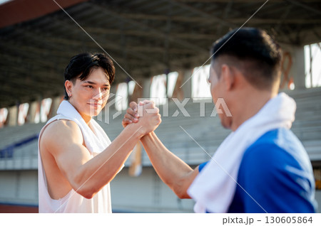Two asian men are joining hands and locking eyes with each other on racetrack. Good sportsmanship. Two asian men are joining hands and locking eyes with each other on racetrack. Good sportsmanship. 130605864