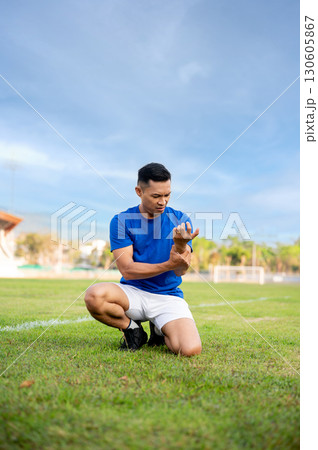 Asian man in blue shirt holding and looking at his arm while kneeling on grass. Arm pain or injury. Asian man in blue shirt holding and looking at his arm while kneeling on grass. Arm pain or injury. 130605867