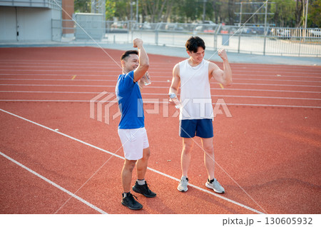 Two asian athlete men holding water bottle and raising their fist while standing on racetrack 130605932