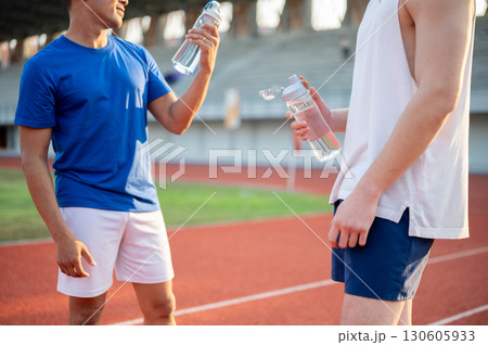 Two asian athlete men are holding their water bottles while talking together on the racetrack. Two asian athlete men are holding their water bottles while talking together on the racetrack. 130605933