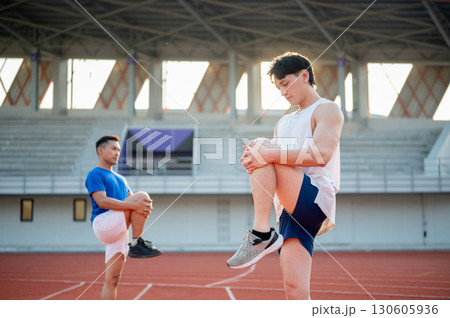 Two asian athlete men are stretching their legs muscles together on the racetrack. Outdoor exercise. Two asian athlete men are stretching their legs muscles together on the racetrack. Outdoor exercise. 130605936