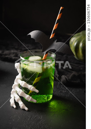 Green Halloween cocktail garnish fun black bat and skeleton hand. Festive drink , spooky setting, featuring eerie elements and playful holiday decor. 130606754