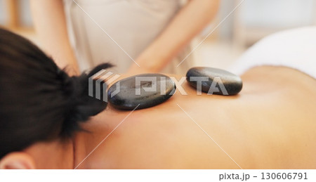 Woman, spa and back with hot stone in closeup, massage or care for professional treatment, muscle and wellness. Girl, masseuse or rock for physical therapy, spine and health at luxury resort for body 130606791