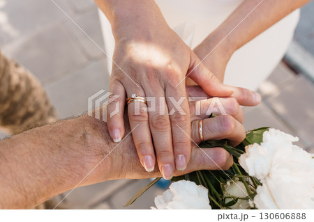 Romantic Wedding Hands Displaying Gold Rings with Bouquet, Intimate Celebration, Close-Up Shot, Warm Lighting, Golden Hour Texture. 130606888