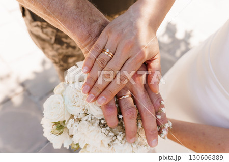 Romantic Hands with Wedding Rings Displaying Love and Commitment with White Roses, Golden Hues, and Warm Tone Photography. 130606889