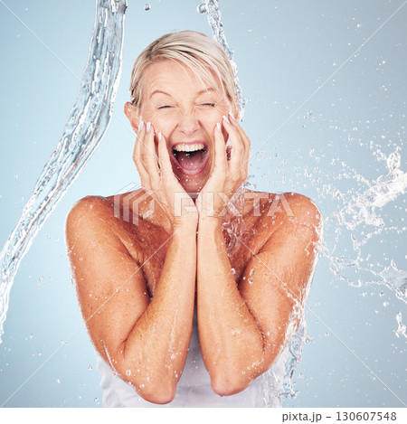 Skincare, excited and portrait of a woman with a water splash isolated on a blue background. Self care, happy and face of an elderly beauty model cleaning her body for wellness on a studio backdrop 130607548