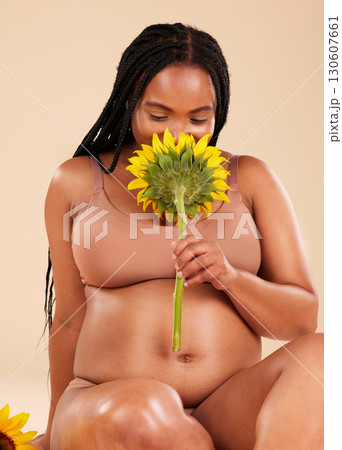 Pregnant, maternity and black woman smelling sunflower happy for a baby in her tummy isolated in brown studio background. Young, motherhood and mother smiling for pregnancy holding a plant 130607661