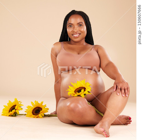 Black woman sitting with flower, pregnant with smile in portrait and beauty, skincare isolated on studio background. Pregnancy glow, mother and nature with natural cosmetic care, health and wellness Black woman sitting with flower, pregnant with smile in portrait and beauty, skincare isolated on studio background. Pregnancy glow, mother and nature with natural cosmetic care, health and wellness 130607666