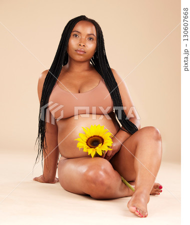 Black woman sitting with flower, pregnant in portrait and beauty with skincare isolated on studio background. Pregnancy glow, mother and nature with natural cosmetic care, health and wellness Black woman sitting with flower, pregnant in portrait and beauty with skincare isolated on studio background. Pregnancy glow, mother and nature with natural cosmetic care, health and wellness 130607668