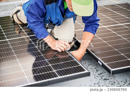 Worker building solar panel system on metal rooftop of house. Man engineer installing photovoltaic solar module outdoors. Alternative, green and renewable energy generation concept. 130608760