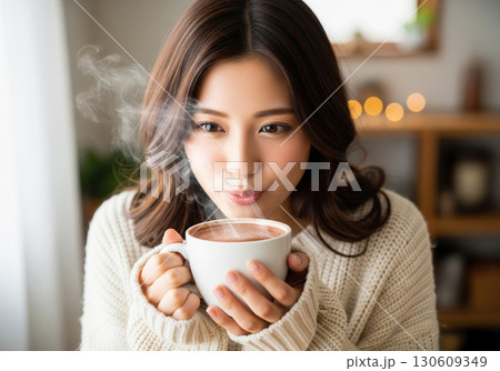 温かいココアを飲むニット姿の女性、優しい秋のくつろぎ時間 130609349