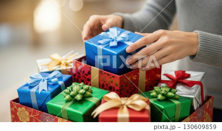 Hands arranging colorful wrapped gifts with ribbons for holiday celebrations Hands arranging colorful wrapped gifts with ribbons for holiday celebrations 130609859