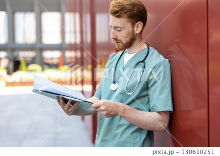 Man in green uniform leaning on wall with open patient records 130610251
