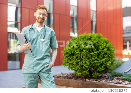 Male doctor holding closed laptop while standing outside clinic Male doctor holding closed laptop while standing outside clinic 130610275