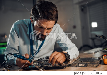 Concentration man, it or soldering motherboard in engineering workshop for night database fixing. Technician, circuit board or tools in repair, maintenance upgrade or information technology industry Concentration man, it or soldering motherboard in engineering workshop for night database fixing. Technician, circuit board or tools in repair, maintenance upgrade or information technology industry 130610326