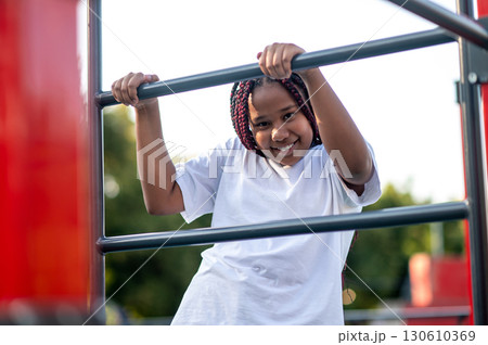 Happy cute girl hanging on the crossbar at the playground Happy cute girl hanging on the crossbar at the playground 130610369